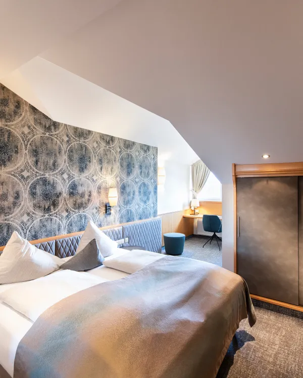 Modernes Hotelzimmer mit Doppelbett, gemusterter Wand, Schreibtisch und Einbauschrank